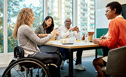 Picture showing a group of colleagues around a table - one of the colleague is in a wheel chair (a woman)
